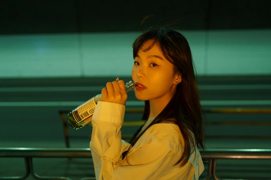 一个年轻的女人站在长椅旁 嘴里含着一瓶水