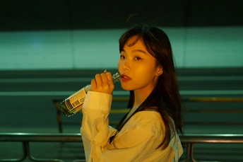 一个年轻的女人站在长椅旁 嘴里含着一瓶水
