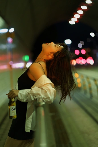一个拿着一瓶啤酒的年轻女子晚上站在街上