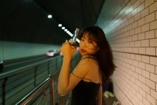 一位身穿黑色连衣裙的年轻女子站在隧道里 手里拿着一杯葡萄酒