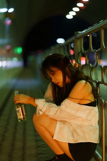 一个拿着一瓶水的年轻女子晚上坐在栏杆上