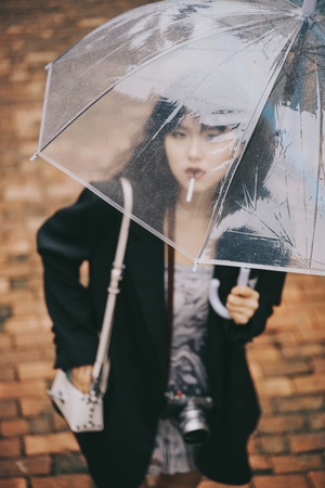 一个拿着透明雨伞的年轻女子拿着相机站在雨中