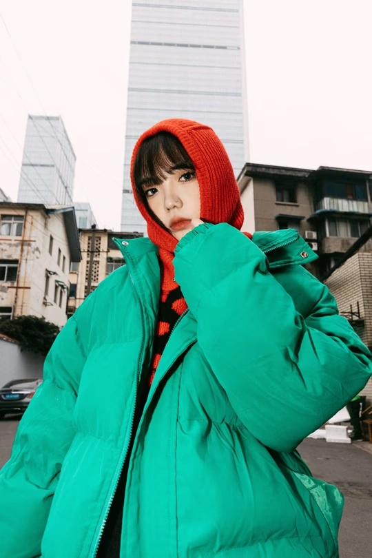 一位戴红帽绿外套带兜帽的妇女站在街上