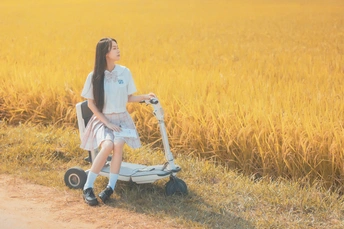 一位年轻美丽的女子穿着白色连衣裙在麦田里骑着滑板车 一个小女孩站在那里。