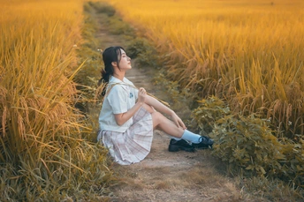 年轻美丽的女子穿着裙子坐在黄色的麦田里