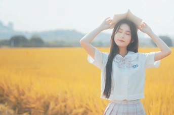 一位年轻女子手里拿着一本书站在一片黄色田野里