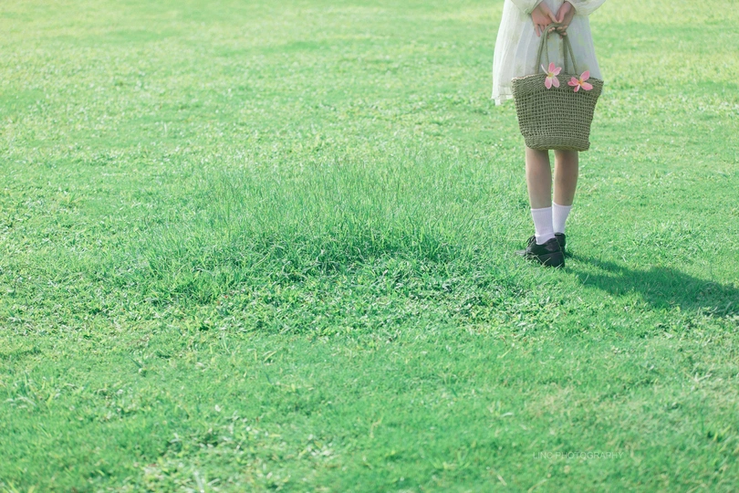 一位穿着白色连衣裙的年轻女子抱着一个花篮 带着小女孩穿过一个草丛丛生的田野。