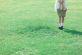 一位穿着白色连衣裙的年轻女子抱着一个花篮 带着小女孩穿过一个草丛丛生的田野。