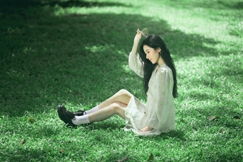一个穿着白裙子的年轻女子坐在树下草地上
