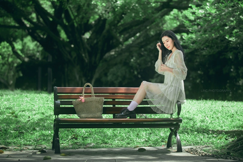 一个穿着连衣裙的年轻女子坐在公园的长椅上 正在打电话。