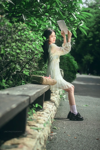 一个穿着连衣裙的年轻女子正在长凳上读书。