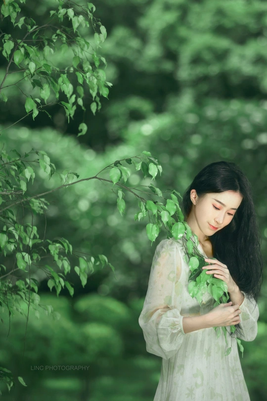 年轻美丽的女子穿着白色裙子 在森林中握着绿色树枝的肖像。