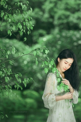 年轻美丽的女子穿着白色裙子 在森林中握着绿色树枝的肖像。