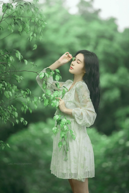 一位穿着白色连衣裙的年轻女子在绿色森林中
