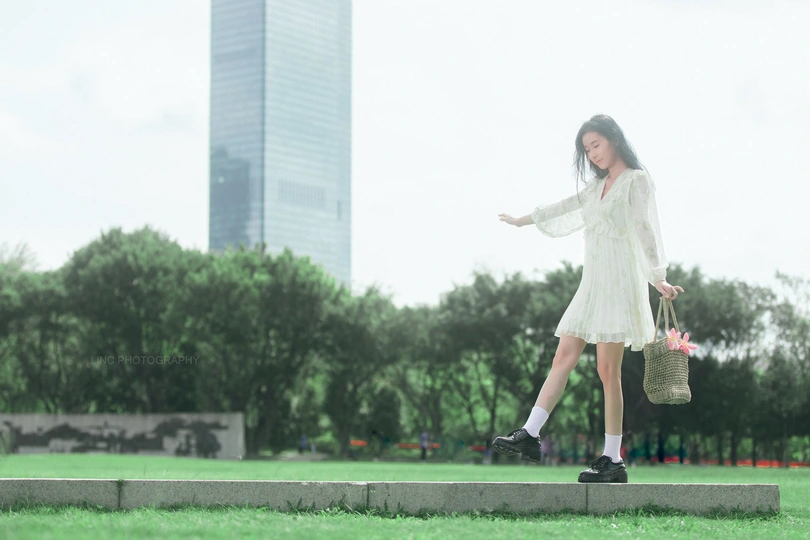 一位穿着白色连衣裙的年轻女子站在公园的草地上
