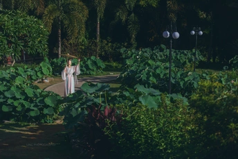 一位穿白衣的女子穿过一个植物花园。