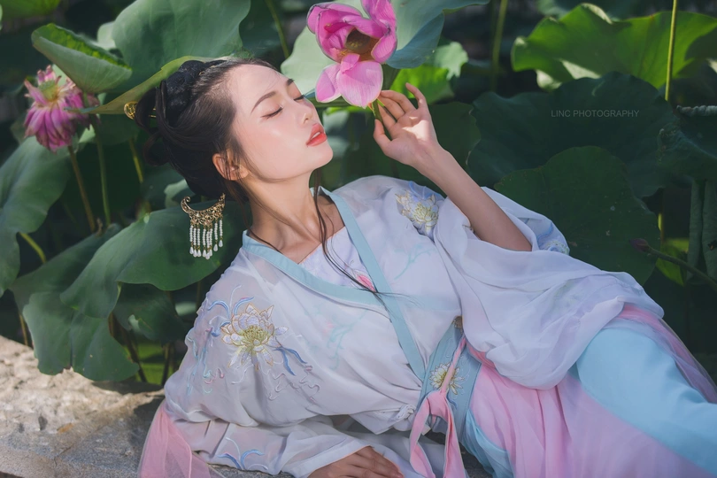 美丽的穿传统中国服装的女士 拿着粉色花。