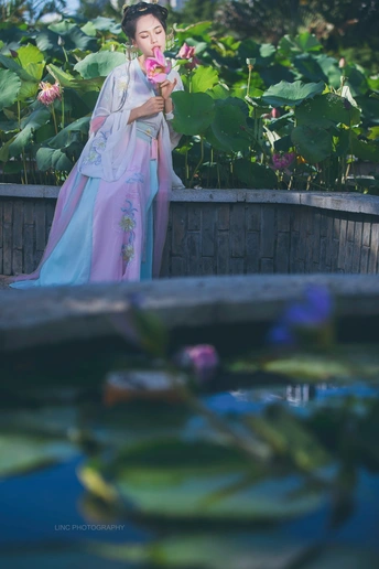 一位美丽的年轻女士穿着一件传统的和服 手里拿着一朵粉红色花 站在池塘边。