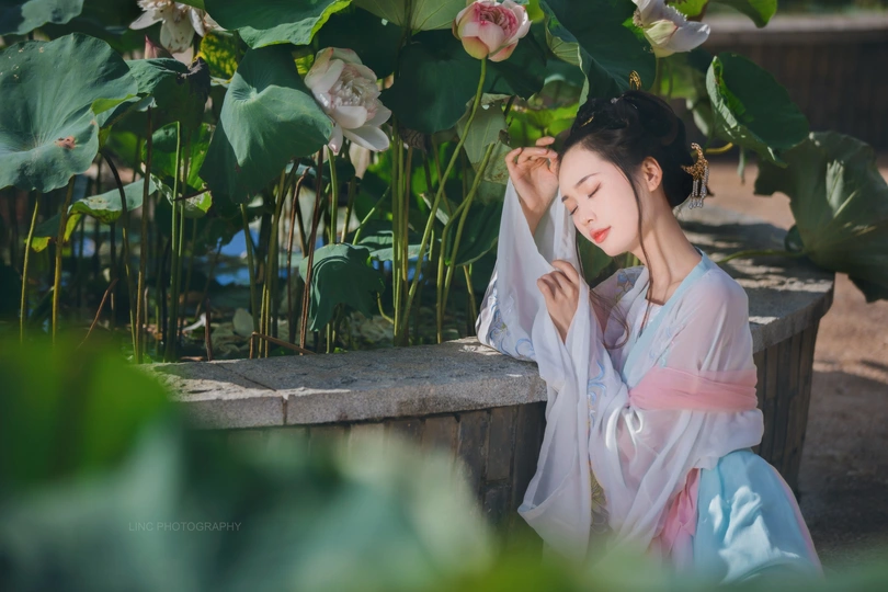 美丽的亚洲女性穿着传统的日本和服坐在水莲花池塘旁边 池塘里盛开着花朵 花园里景色宜人。