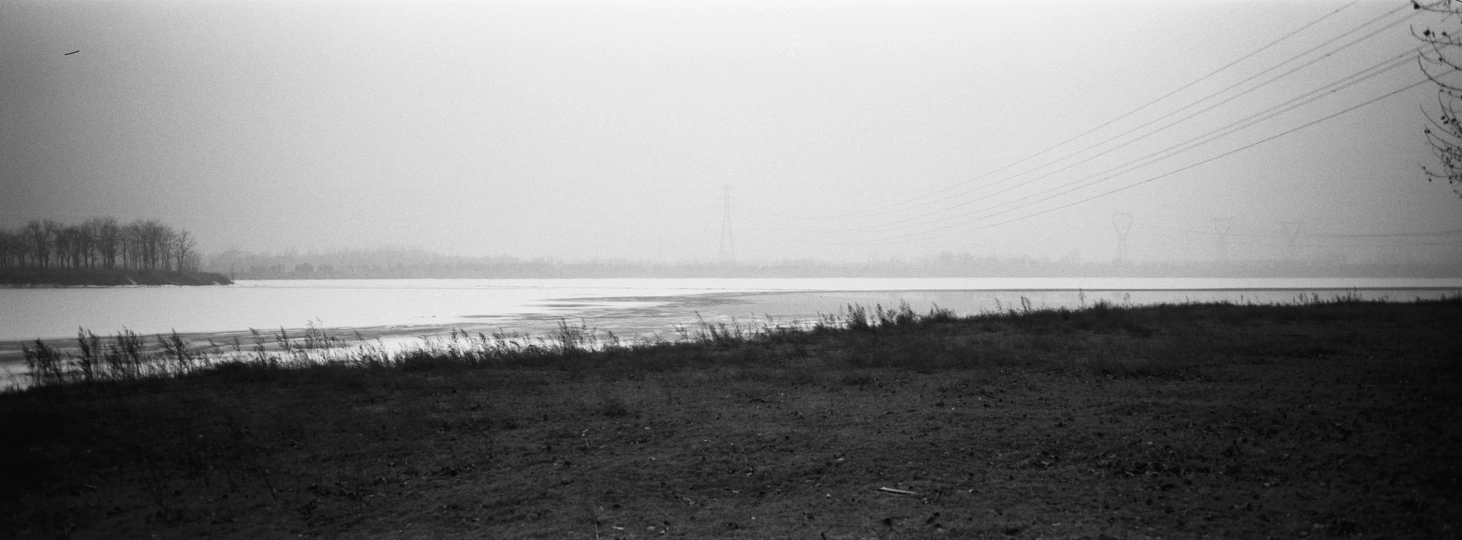 一张黑白照片 展示了旁边有条河 远处有电线杆。
