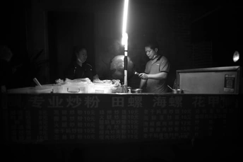 一张黑白照片 夜晚 人们坐在桌子旁 桌子上有一盏灯在柜子上。