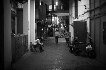 一张黑白照片 夜晚 一条狭窄的巷子 人们坐着 有些人骑着自行车。