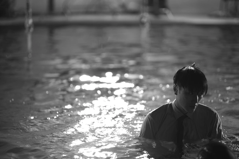 一个穿领带的年青男子站在一个水坑里 而另一个人在水坑里游泳。