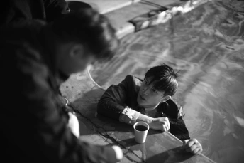 一个穿着黑白衣服的小女孩正在喝杯子里的东西 一个年轻男孩坐在游泳池边