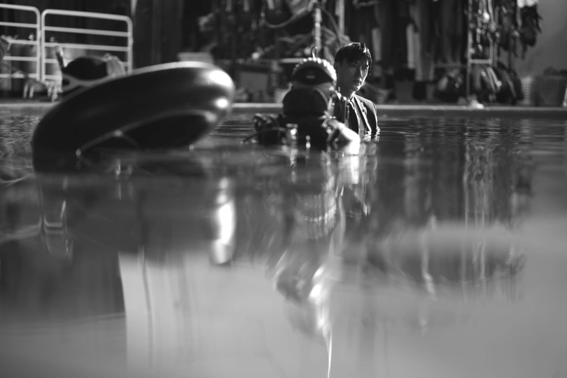 黑白照片 游泳池里有人 一个年轻男孩坐在游泳池边缘