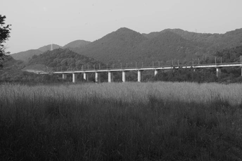 一张黑白照片 火车穿越田野 背景是山脉。