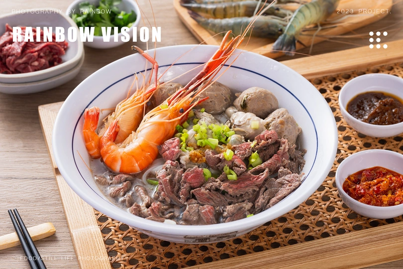 一个木制桌子上有筷子、盘子和包含肉类、虾和酱汁的食物。