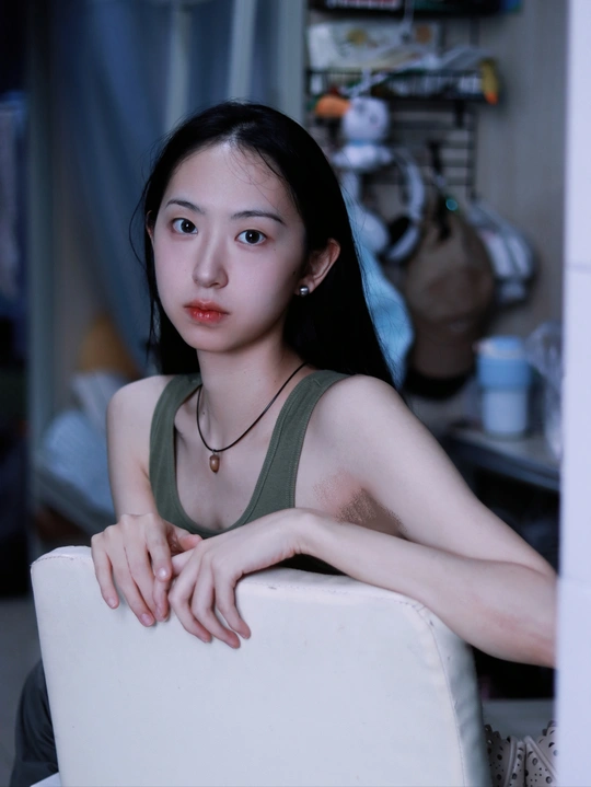 一位年轻女子坐在白色椅子上 桌子旁 正看着相机。