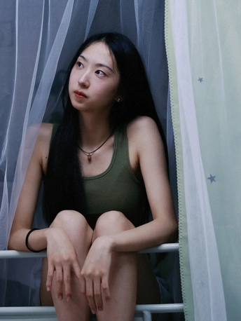 一位穿着绿色衣服的年轻女子坐在窗前帘子后面向外看