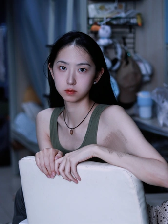 一个年轻女子坐在一个凌乱的房间里 坐在白色的椅子上 看着相机。