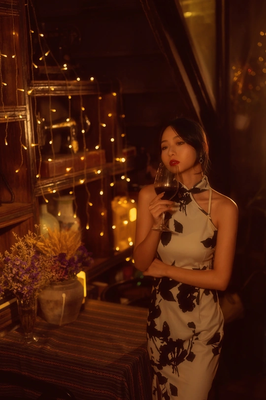 一个穿着连衣裙的年轻女子拿着一杯红酒在灯光昏暗的房间里摆姿势