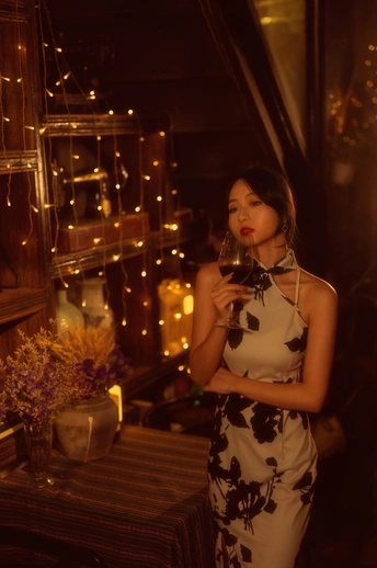 一个穿着连衣裙的年轻女子拿着一杯红酒在灯光昏暗的房间里摆姿势