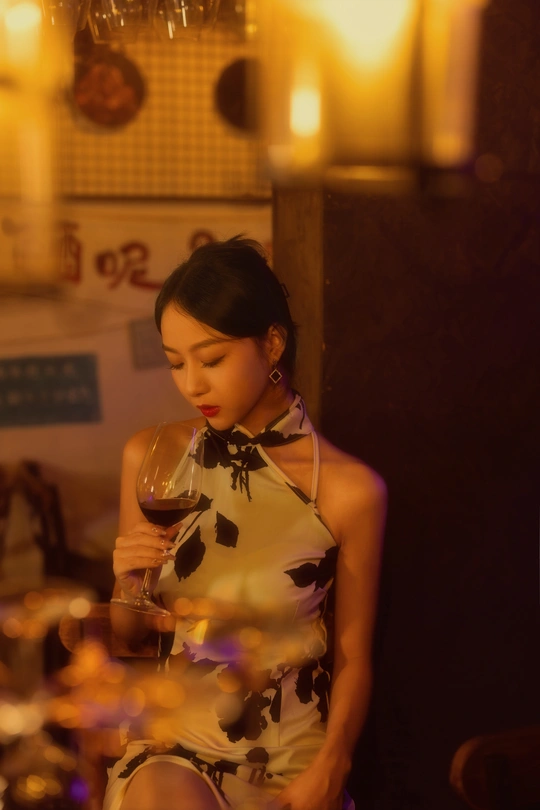 一个穿着连衣裙的年轻女子拿着一杯红酒站在一张放着蜡烛的桌子前