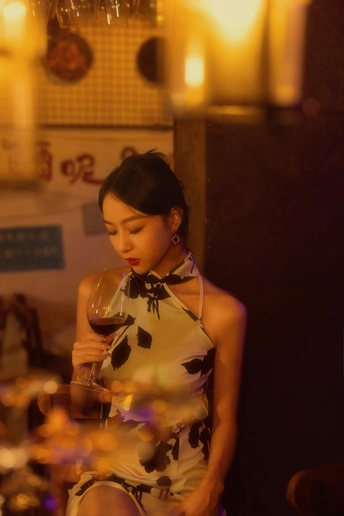 一个穿着连衣裙的年轻女子拿着一杯红酒站在一张放着蜡烛的桌子前