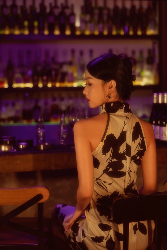 一个穿着连衣裙的年轻女子坐在酒吧的长椅上 手里拿着几瓶饮料