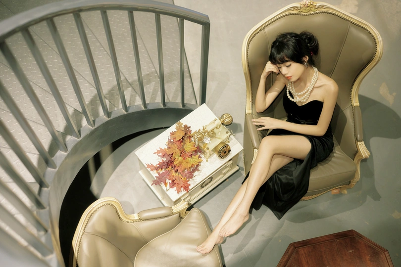 一个穿着黑色连衣裙的年轻女子坐在螺旋楼梯上的椅子上