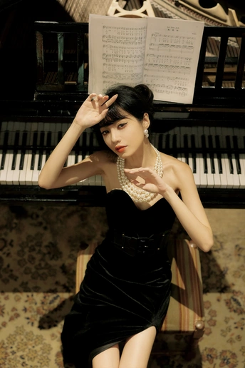 一个穿着黑色连衣裙的年轻女子站在钢琴前