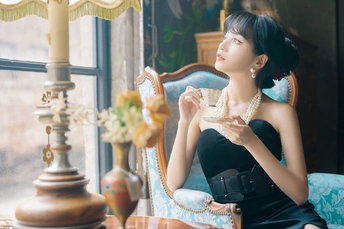 一个穿着黑色连衣裙的年轻女子坐在窗前的椅子上喝着茶