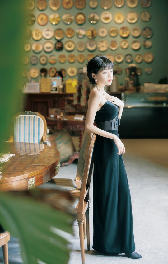 一位身穿黑色长袍的年轻女子在一间有桌椅的房间里摆姿势