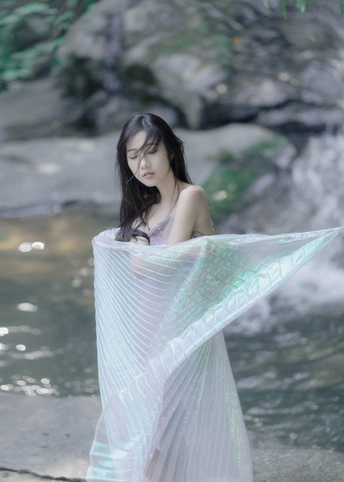 一位身穿白色连衣裙、披着粉色披肩的美丽年轻女子站在溪流中