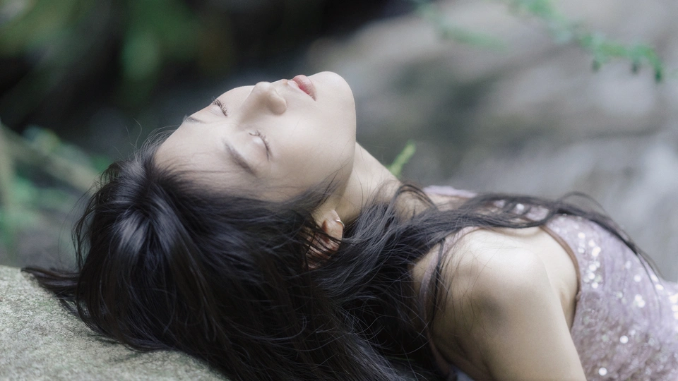 一个穿着漂亮连衣裙的年轻女子闭着眼睛躺在岩石上