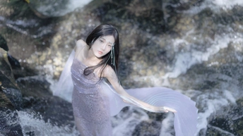 一个穿着紫色长裙的年轻女子站在河里或小溪里