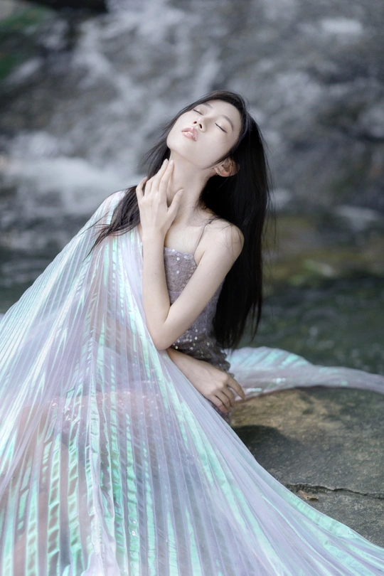 穿着长裙的漂亮年轻女子坐在瀑布附近的岩石上