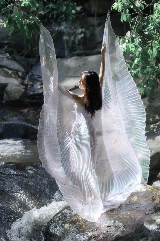 站在小溪或河里的岩石上的一个穿着带翅膀的白色连衣裙的年轻女子