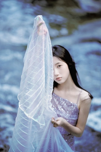 一个穿着蓝色连衣裙和白色围巾的年轻女子站在小溪边