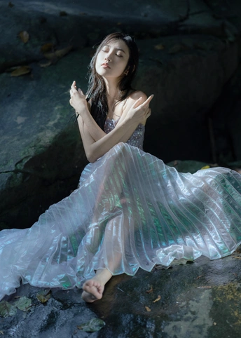 穿着蓝色连衣裙的年轻美女坐在水中的岩石上